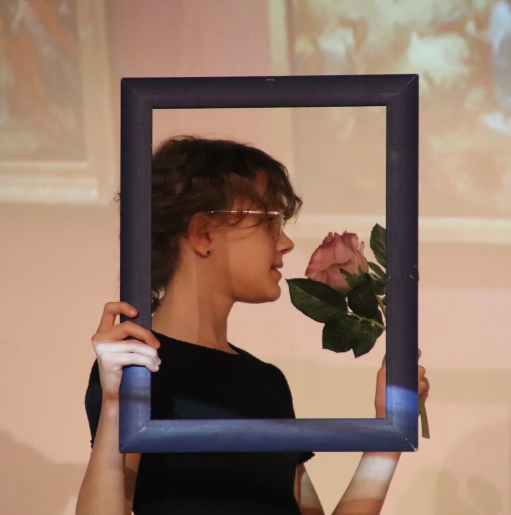 Junge Frau mit Brille hält Rahmen und duftet an rosa Rose